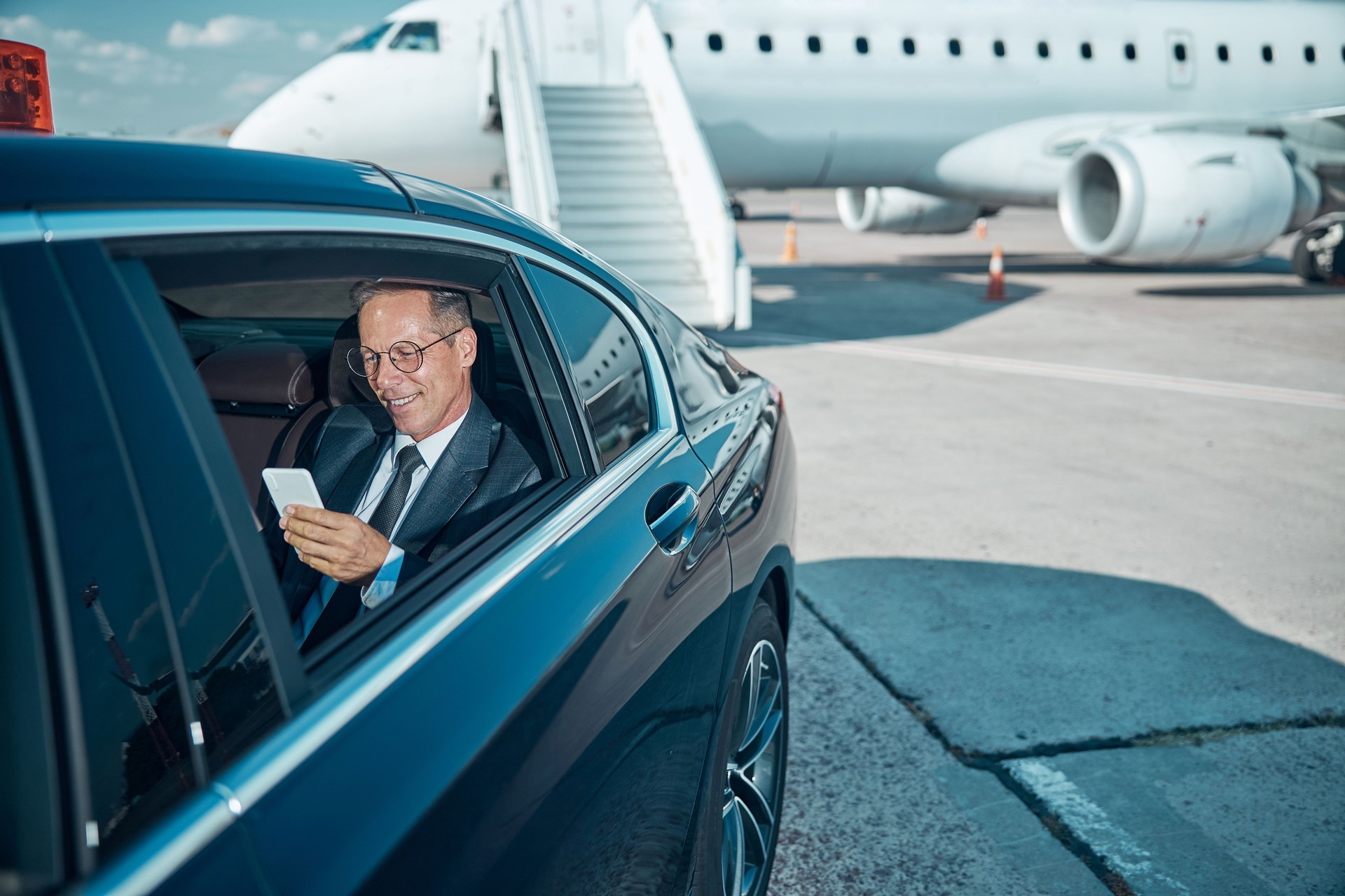 Empresário alegre com smartphone no carro no aeroporto